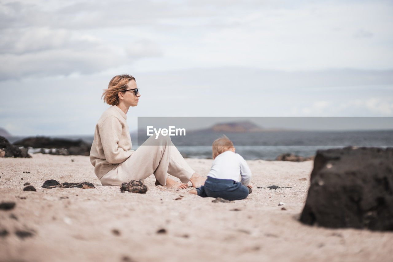 side view of woman sitting at beach against sky