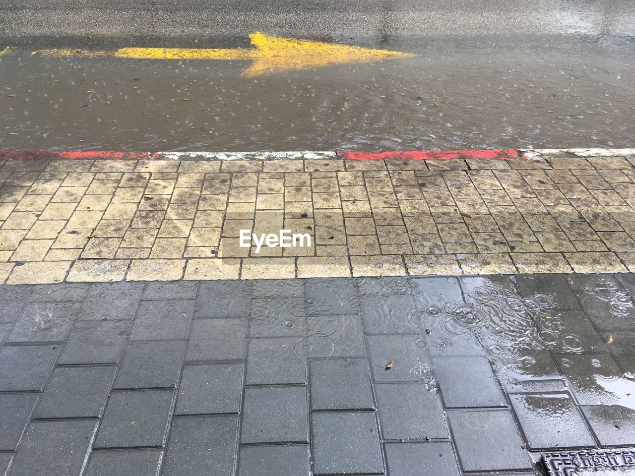 Road fluded by rain yellow arrow pointing left traffic signs and marks white and red line puddle 