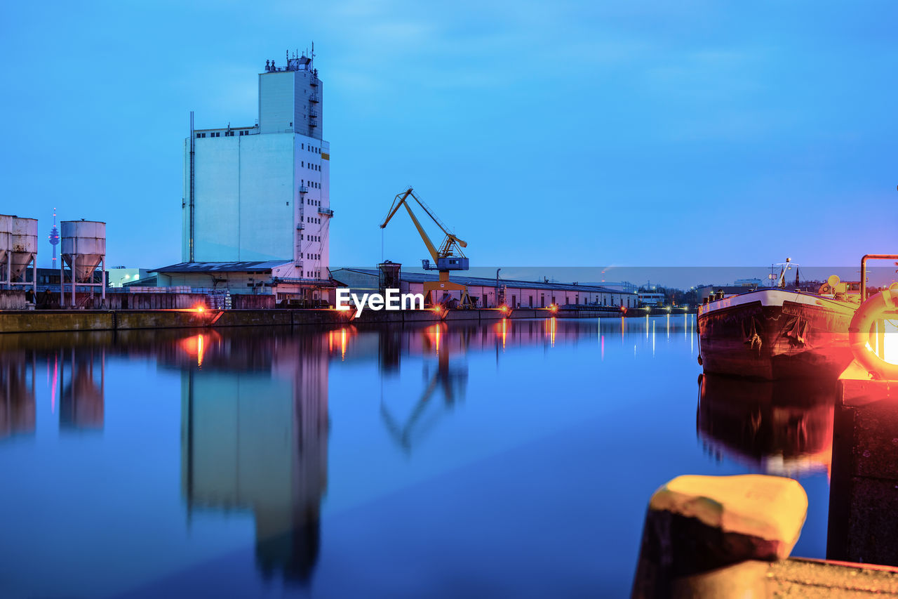 Reflection of illuminated pier on river against sky