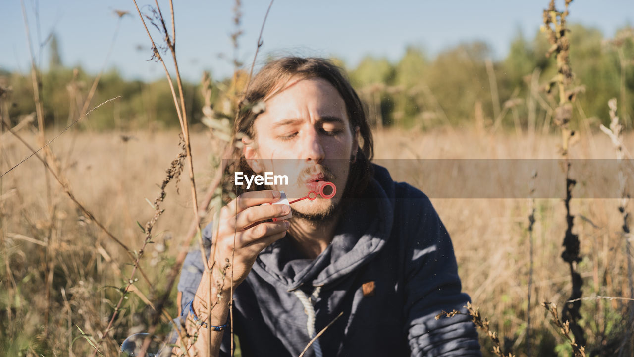 Young man blowing bubble wand by plants on land