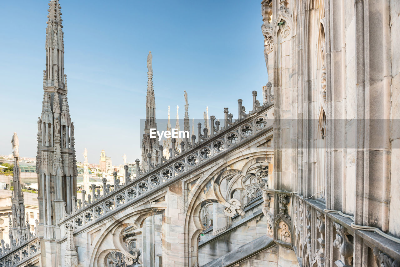 View to spires and statues on roof of duomo through ornate marble fencing. milan, italy