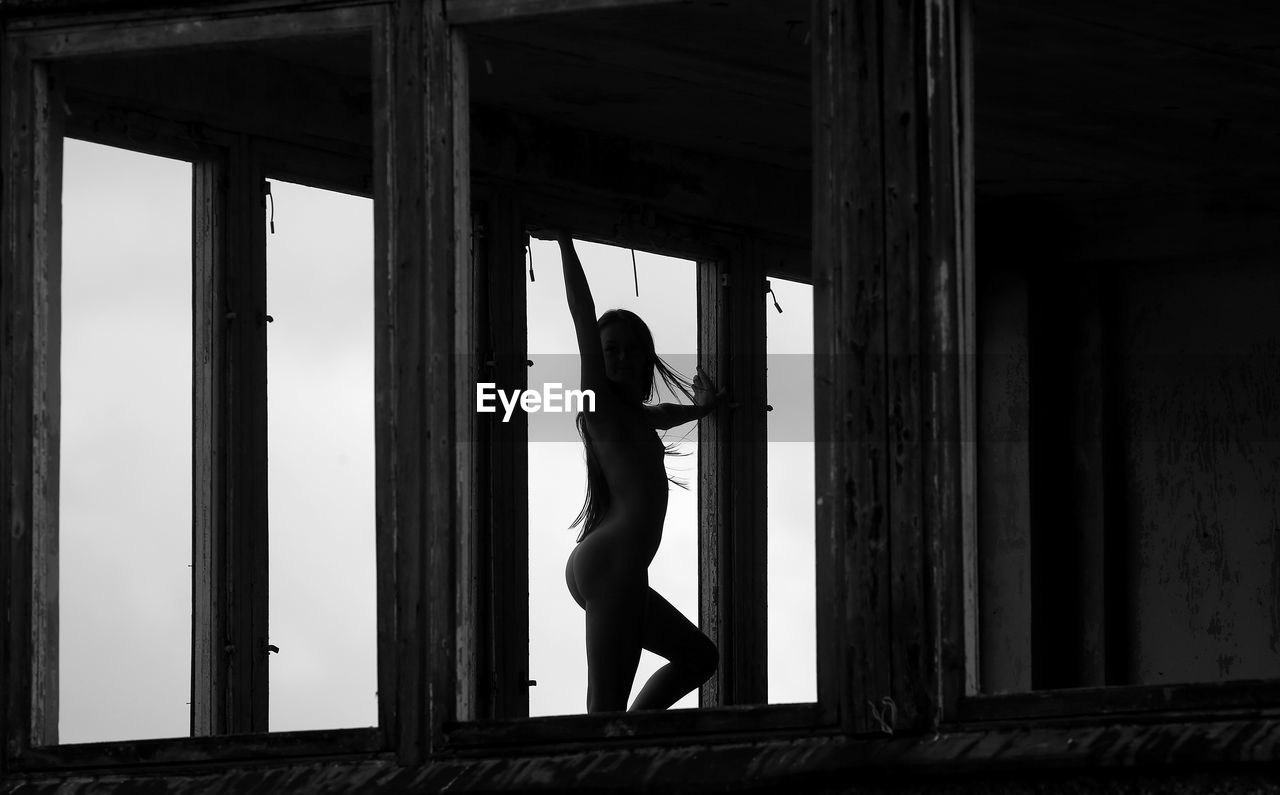 Naked young woman standing by window