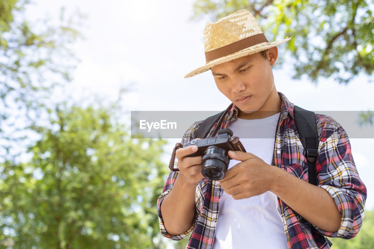 Man holding camera while standing against tree