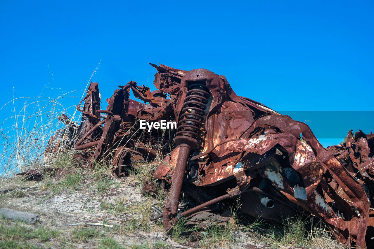 LOW ANGLE VIEW OF RUSTY ABANDONED STRUCTURE AGAINST BLUE SKY