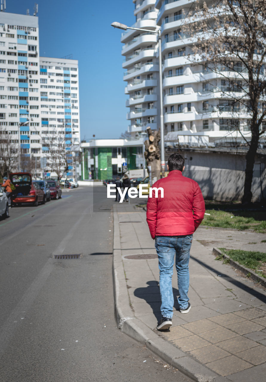 REAR VIEW OF PERSON WALKING ON ROAD BY BUILDINGS