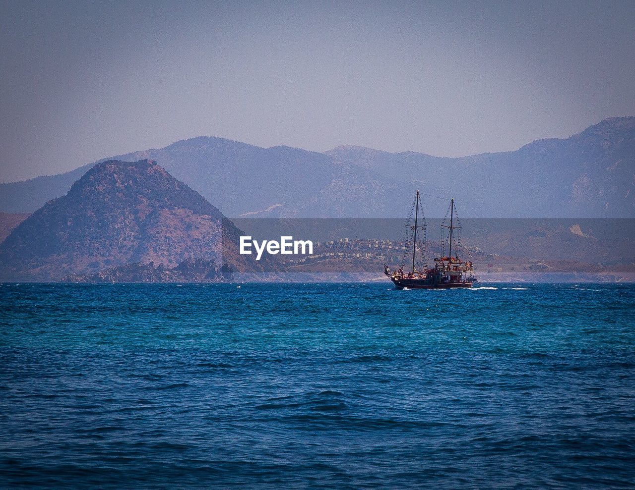 SAILBOAT SAILING ON SEA AGAINST MOUNTAINS