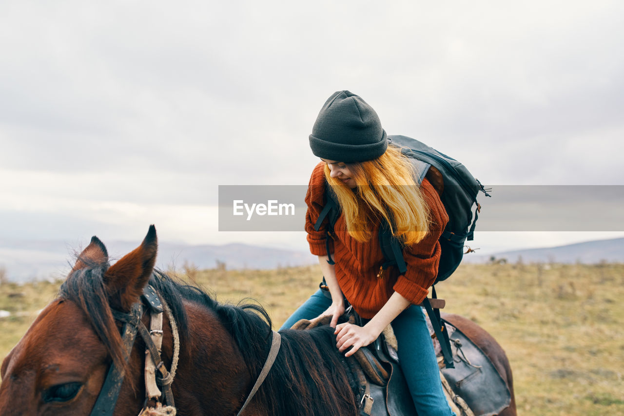 MAN RIDING HORSE ON FIELD AGAINST SKY