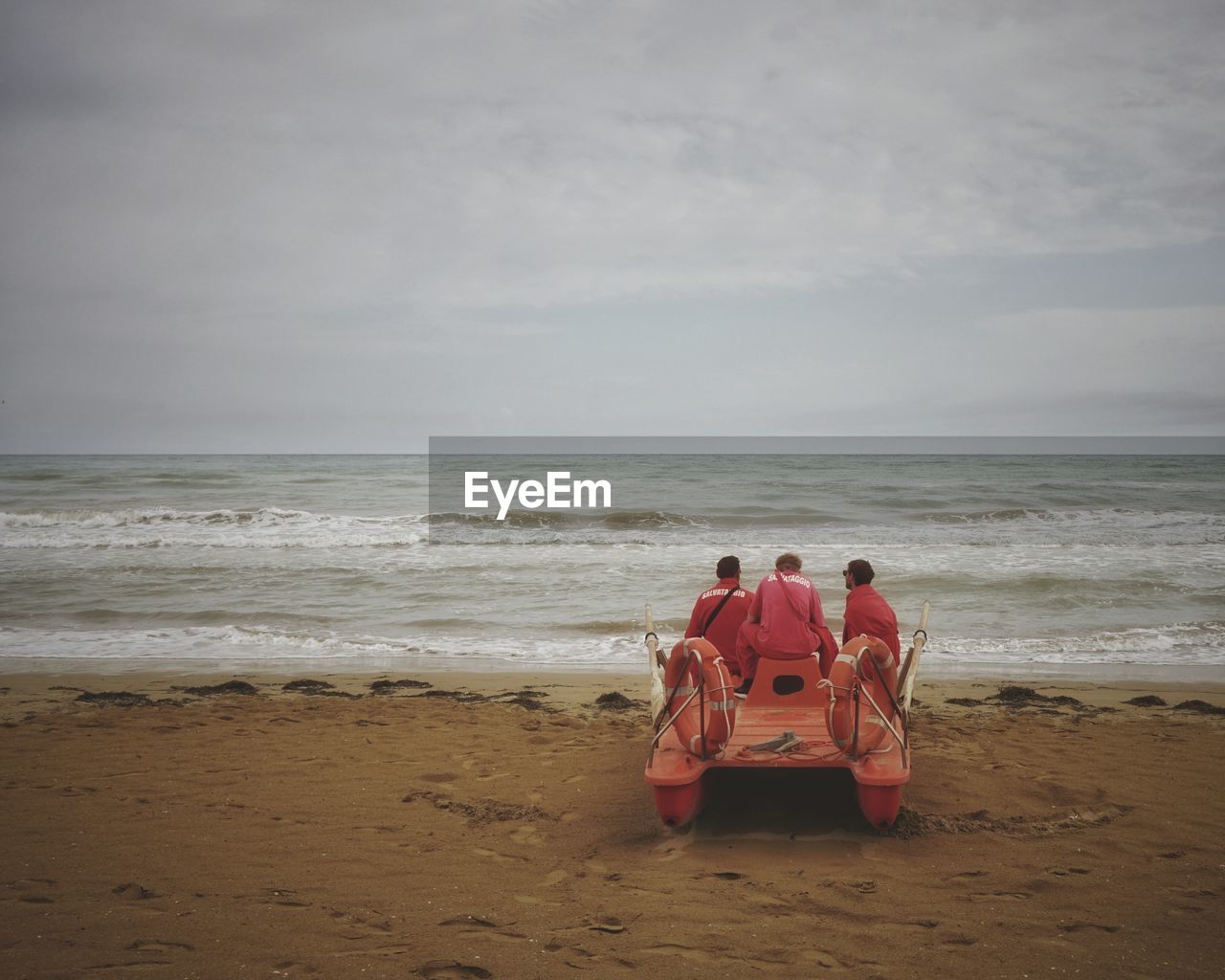 Men sitting on lifeboat at beach against sky