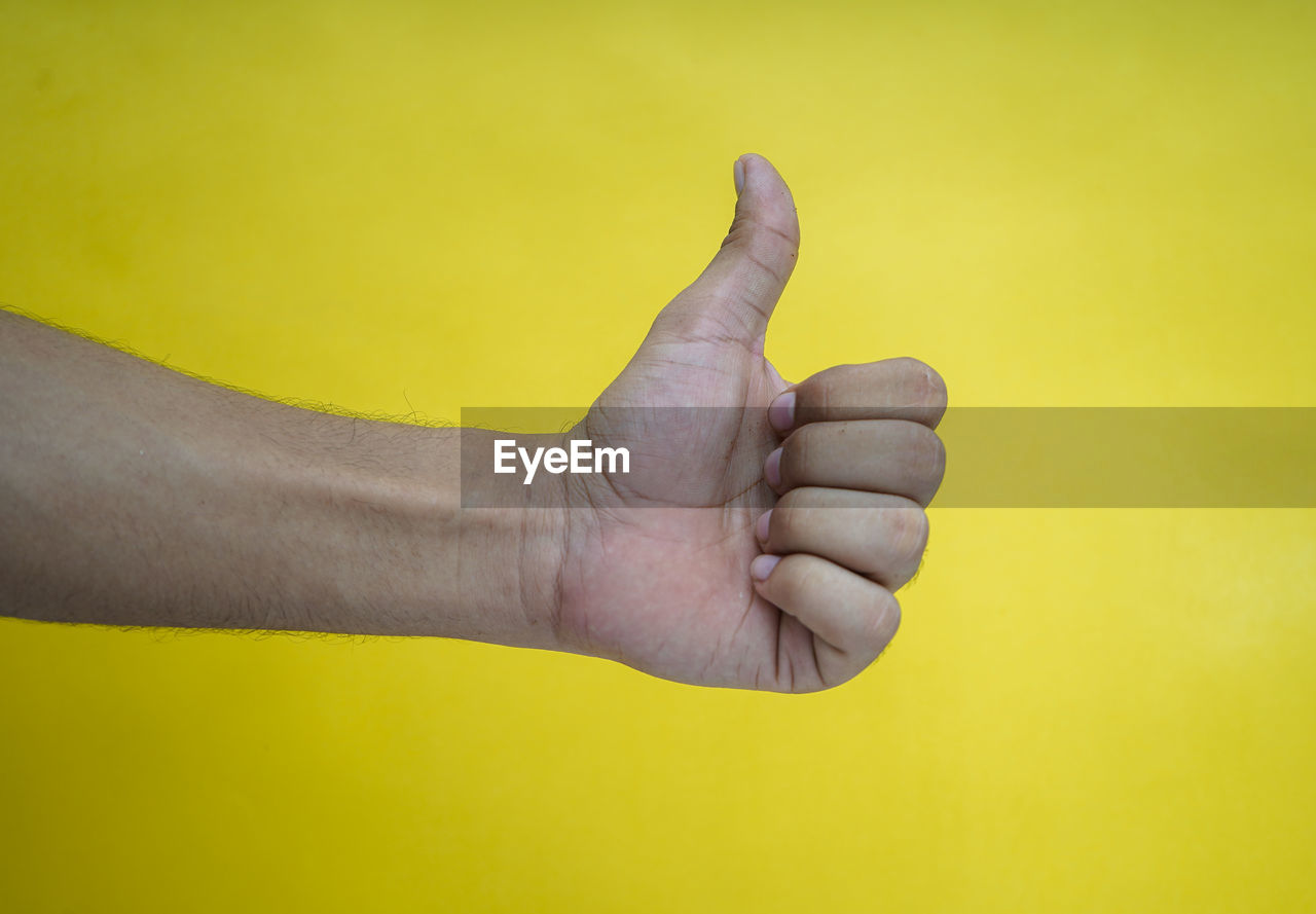 CLOSE-UP OF HUMAN HAND AGAINST YELLOW COLORED BACKGROUND