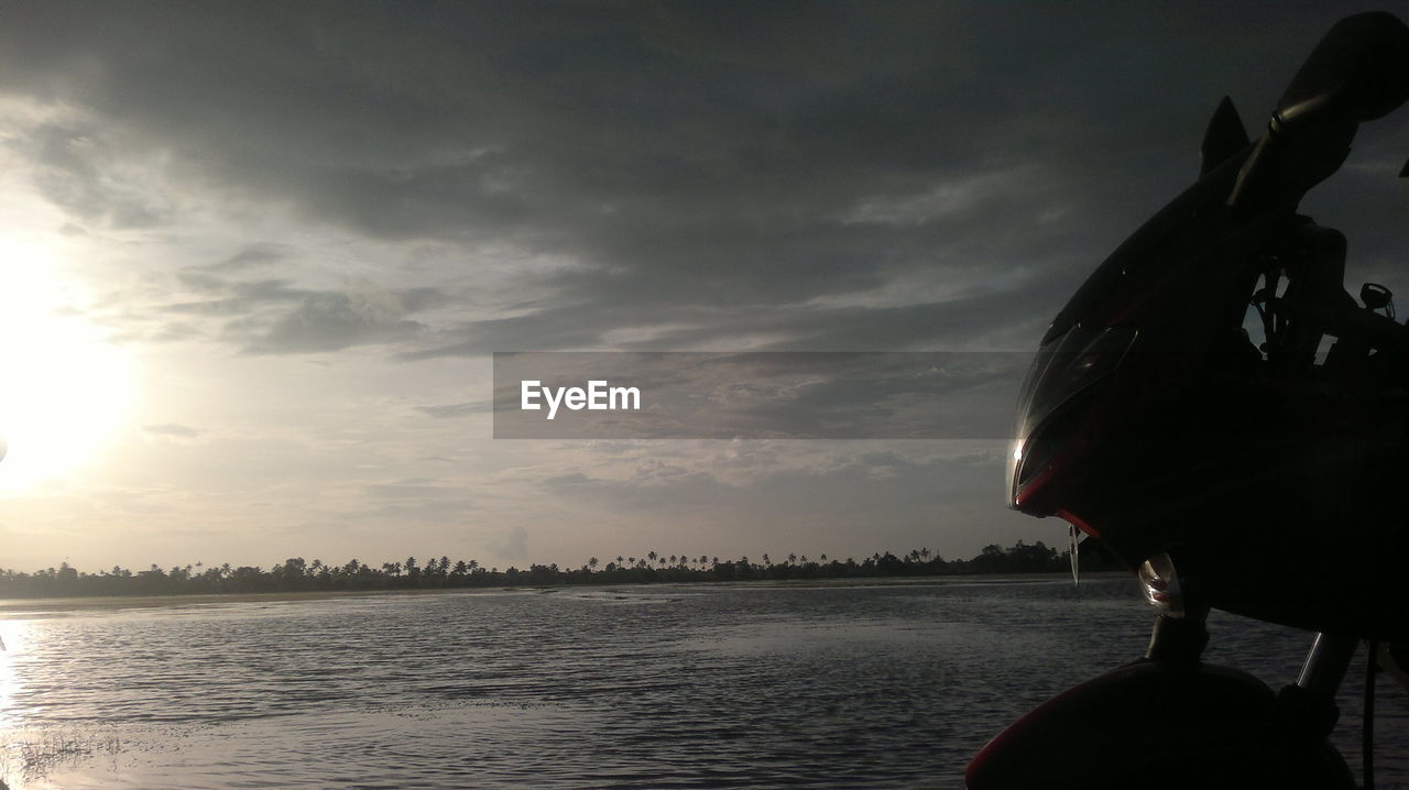 Cropped hand of man on motorcycle by lake against cloudy sky