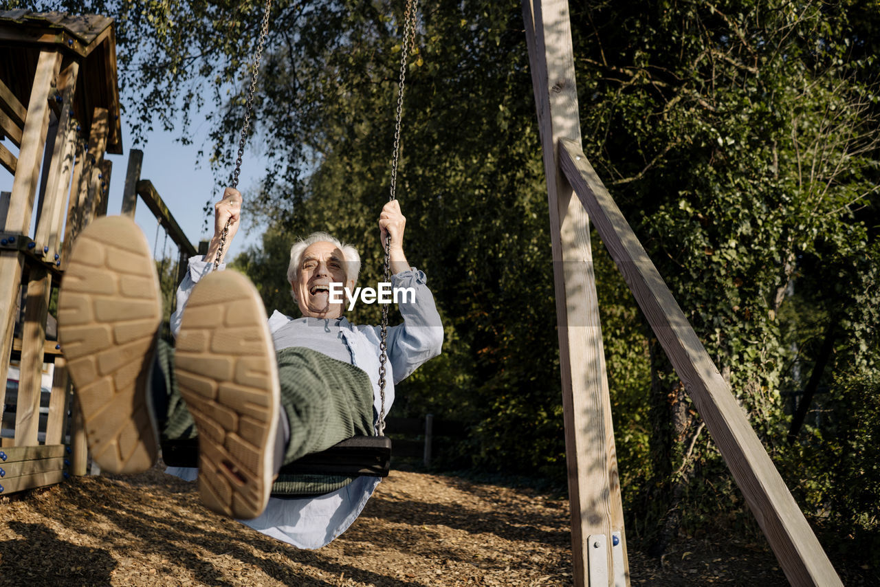 Senior man sticking out tongue while playing on swing at park