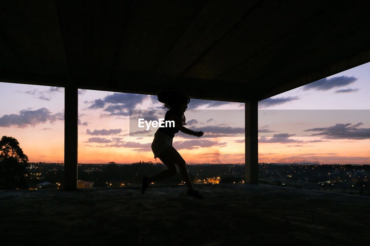 Full length of woman jumping in building during sunset