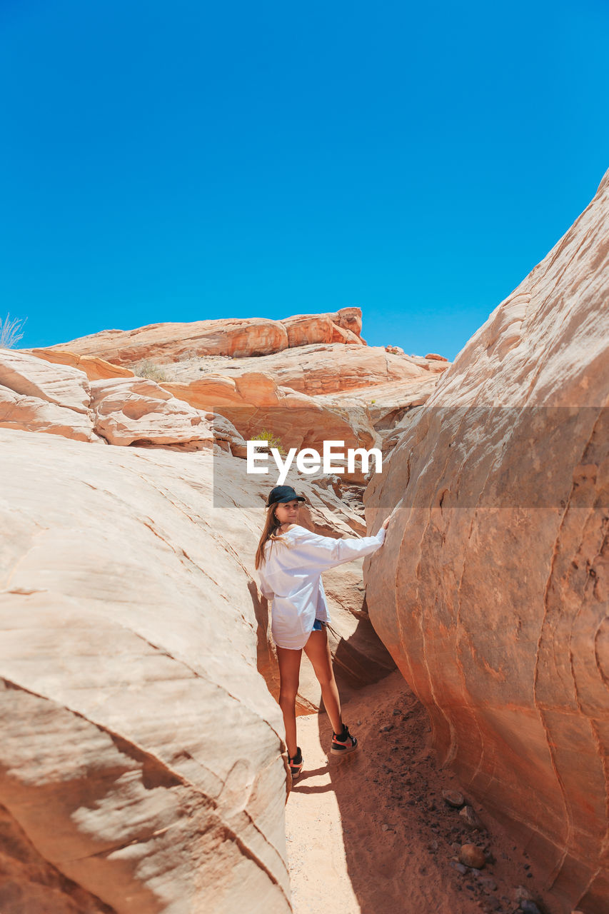 rear view of man standing on rock formations against clear blue sky