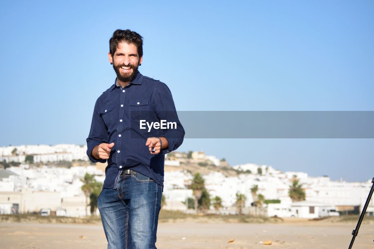 Portrait of smiling man gesturing standing against blue sky