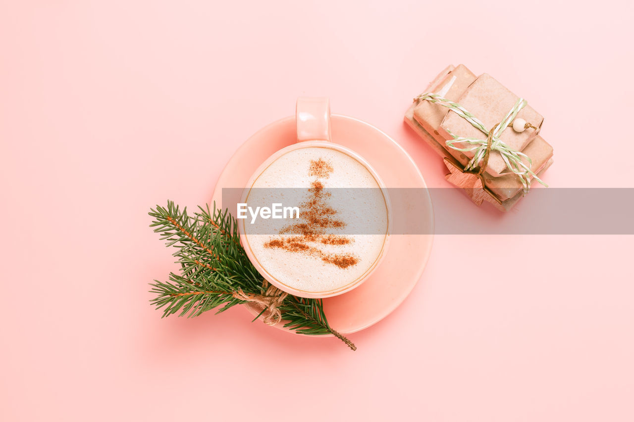 Top view of cup of latte with art in shape of christmas tree on pink background