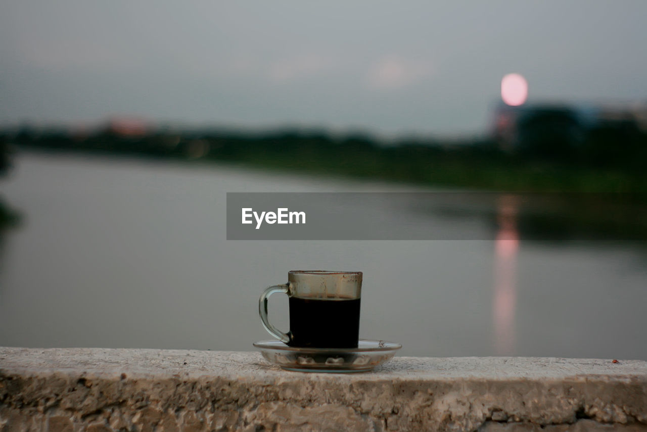 Close-up of coffee cup against lake