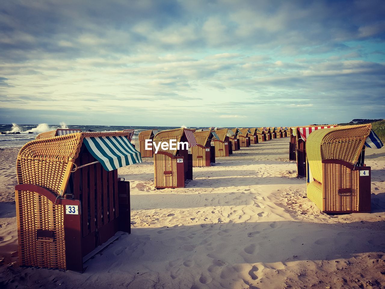 Hooded chairs on beach against sky