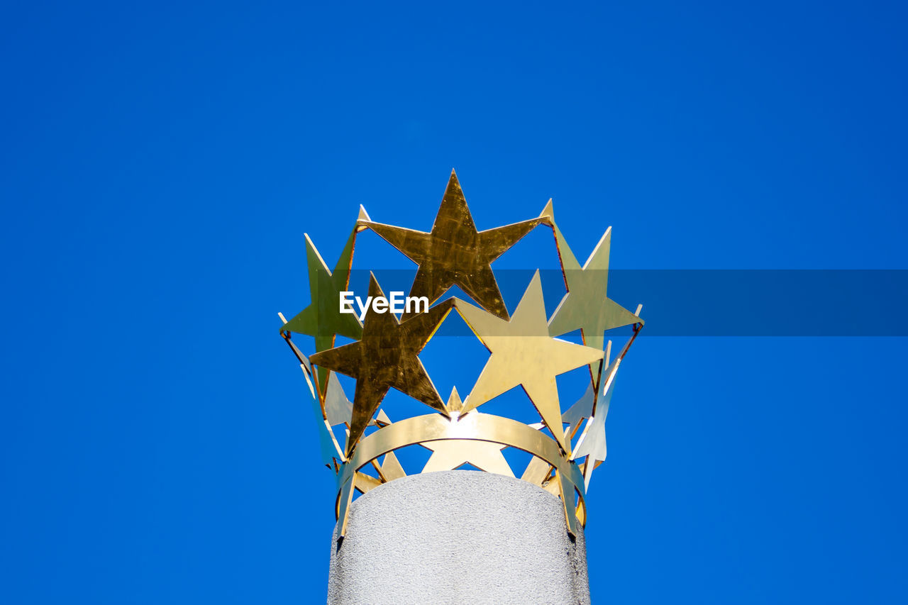 Crown of golden stars on a column with blue sky as a background