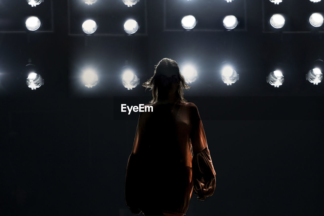 Rear view of woman standing against illuminated lights