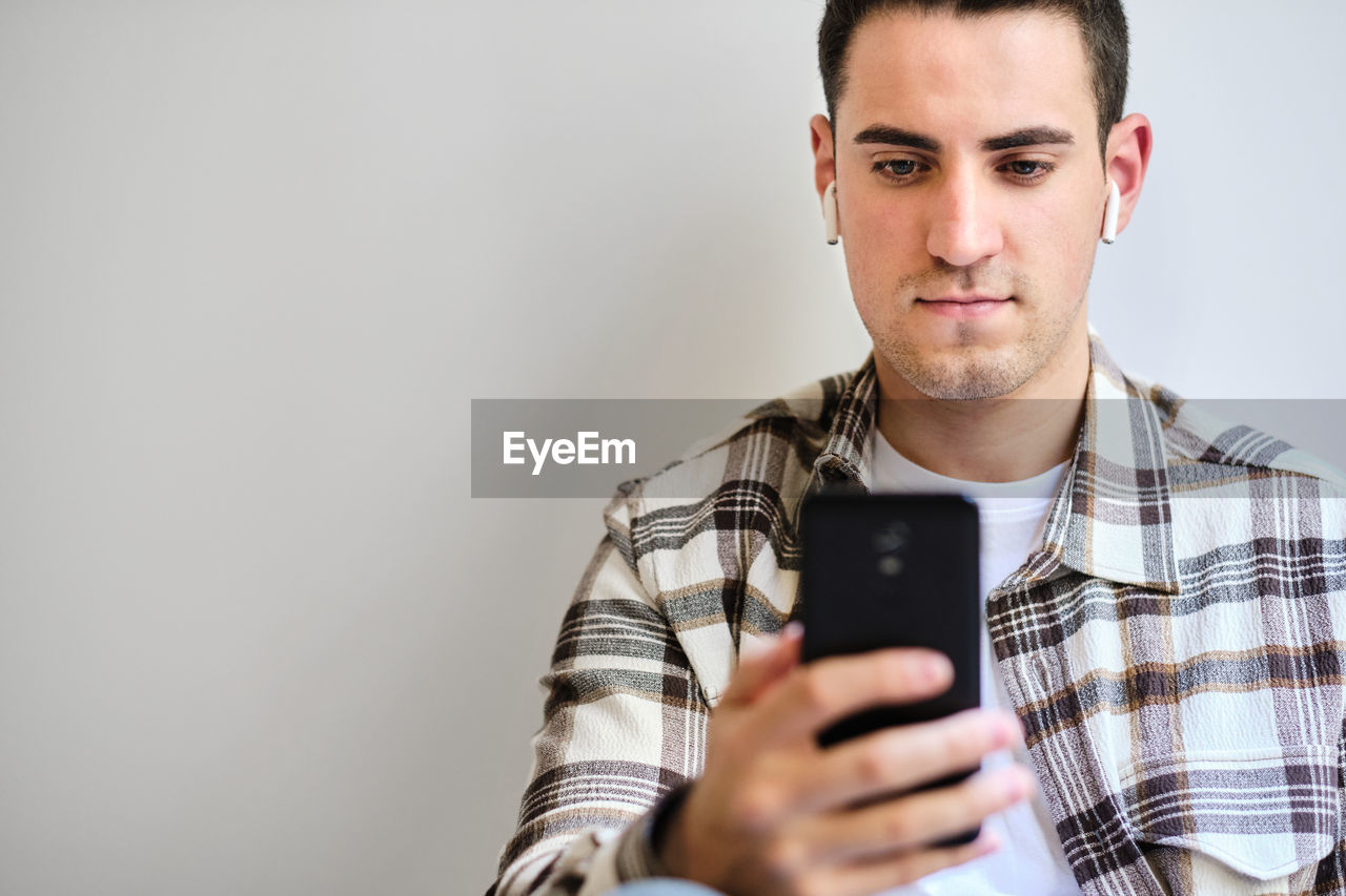 Young man with earphones looking at smartphone. chilling at home. copy space.