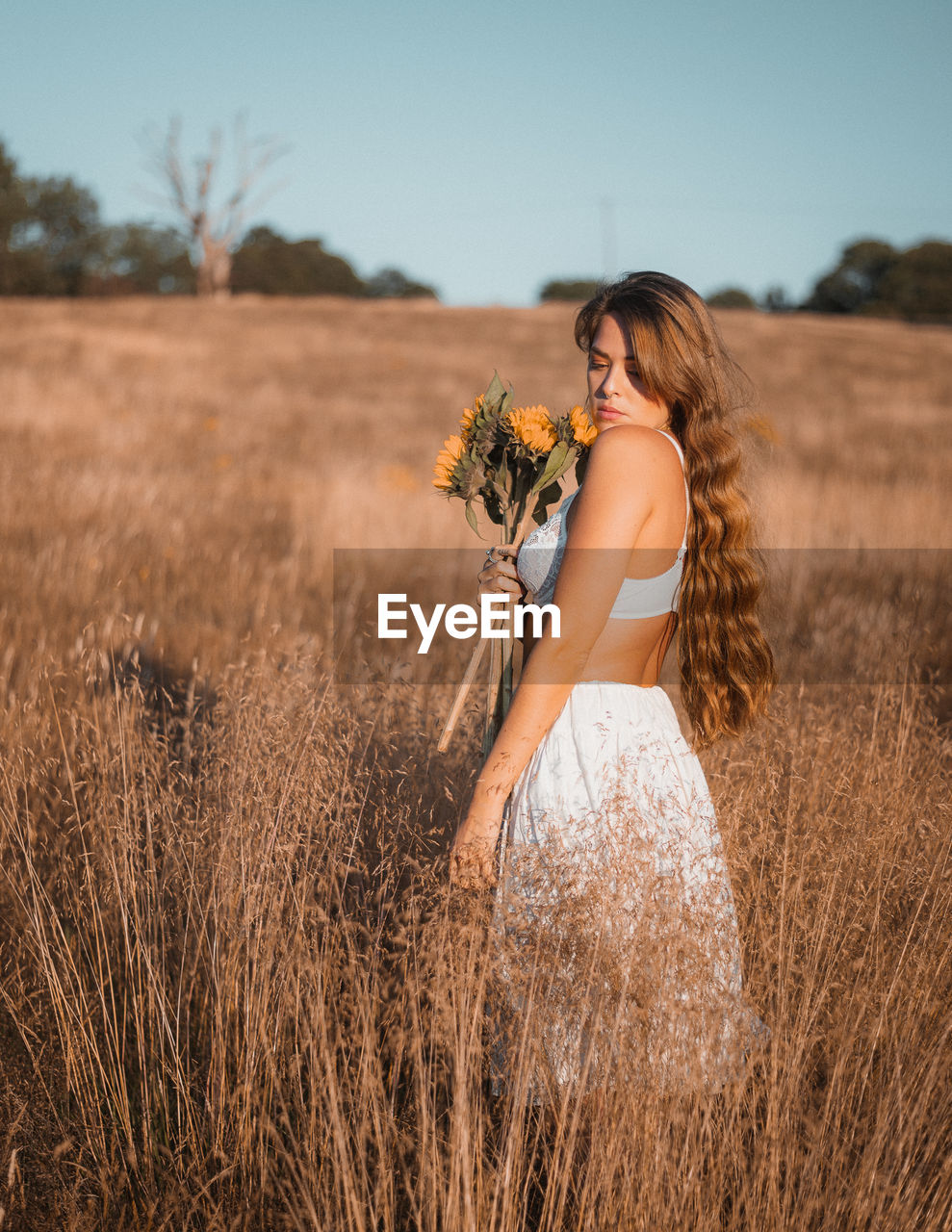 Young woman with flowers standing by plants against sky