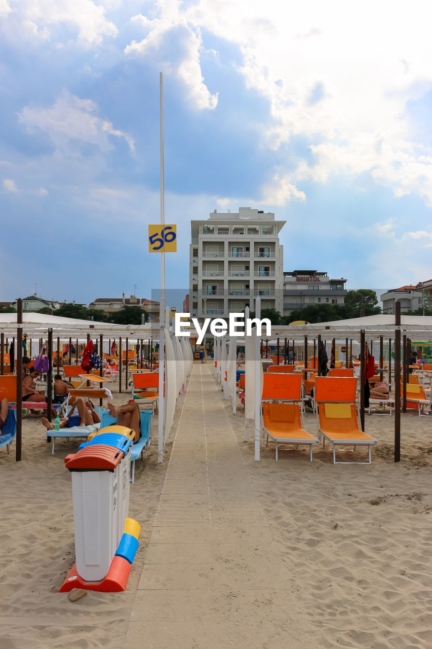 Walkway amidst deck chairs at beach against sky