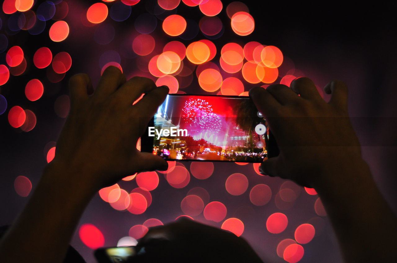 Close-up of person photographing fireworks at night
