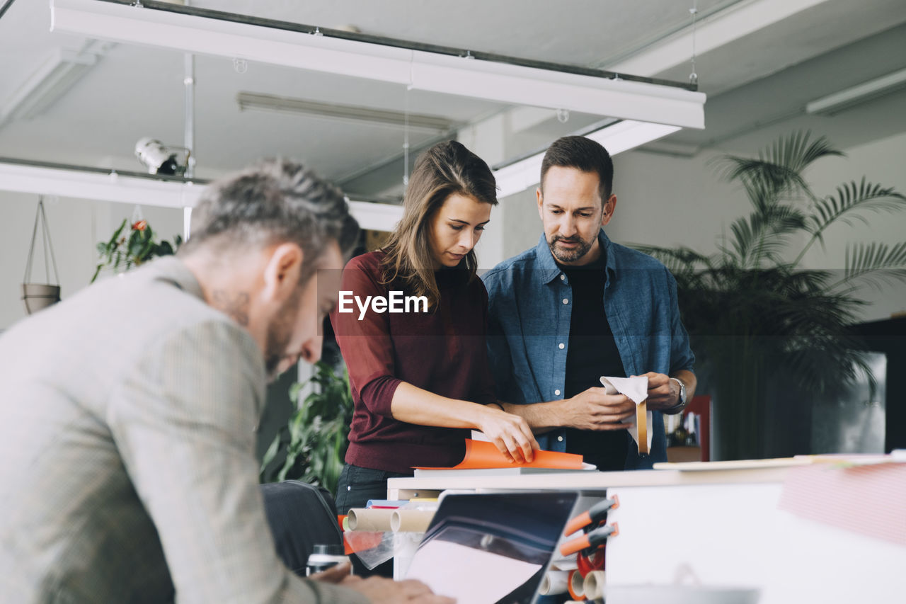 Businessman and businesswoman discussing while male colleague working on laptop in creative office