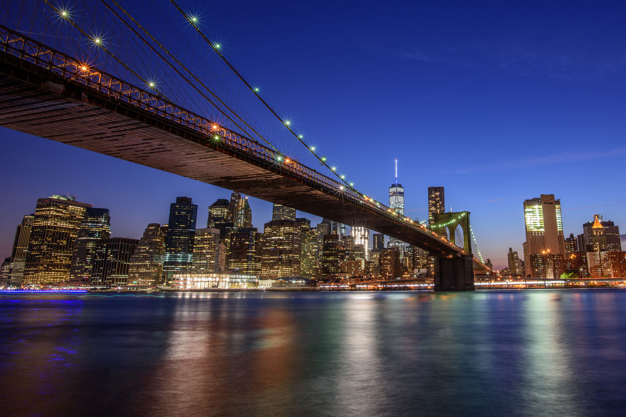 Illuminated brooklyn bridge over east river against sky