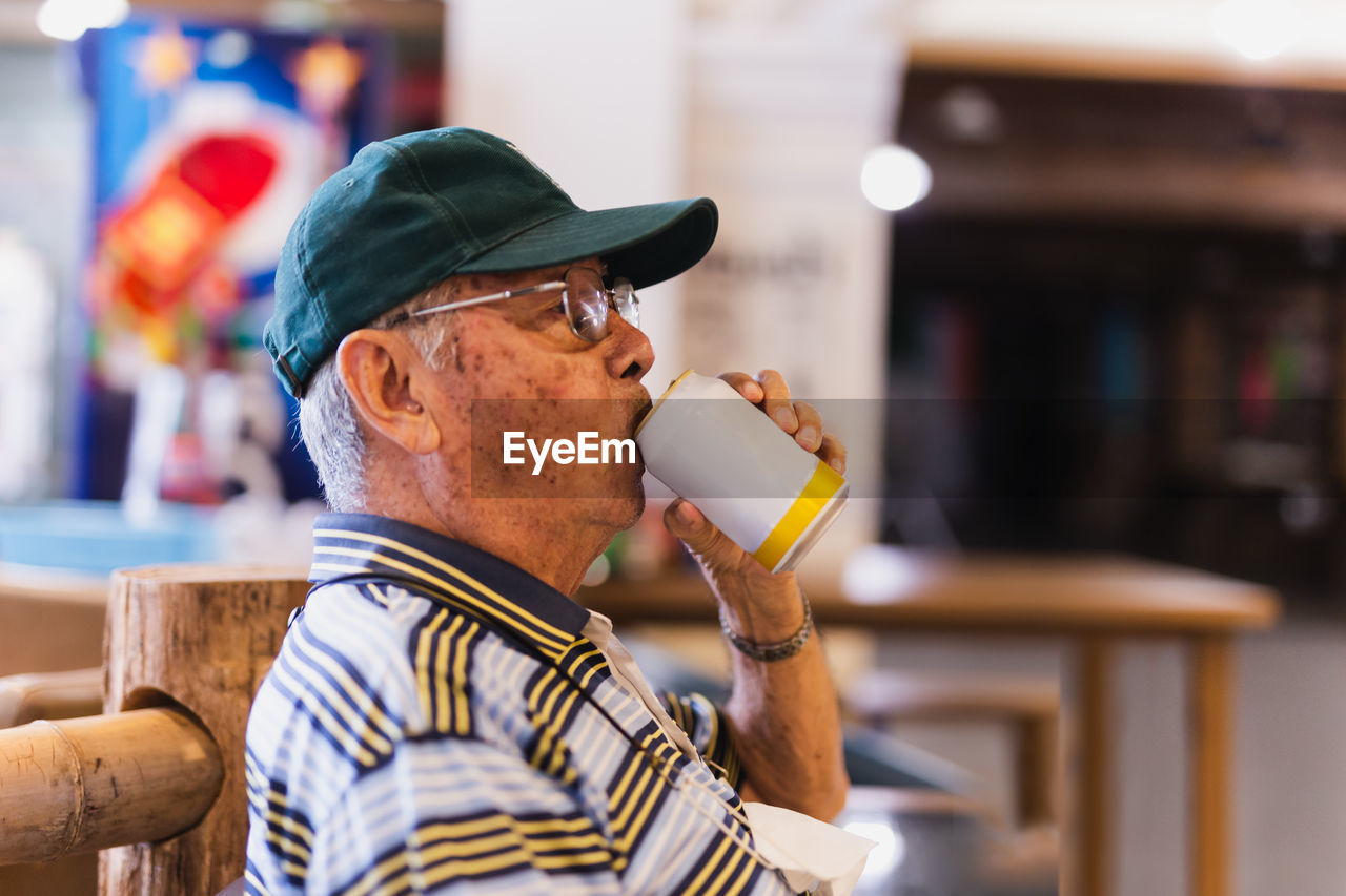 Side view ofsenior man drinking beer while sitting in a chair outdoor.