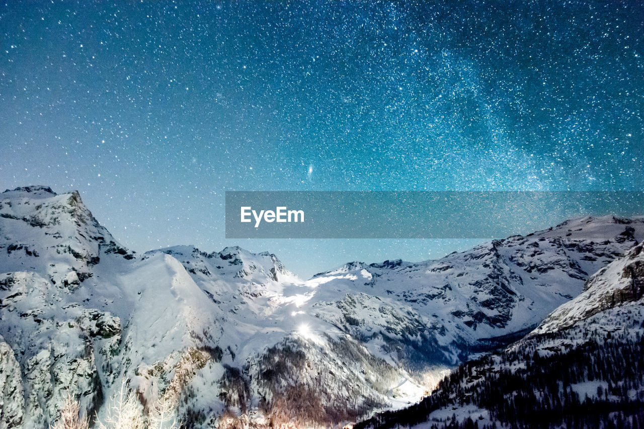 Scenic view of snowcapped mountains against stars at night