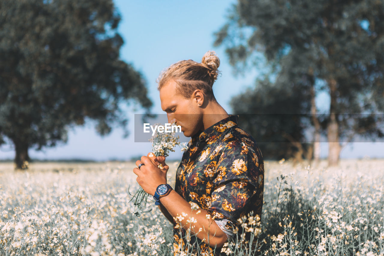 Man smelling flowers while standing against tree