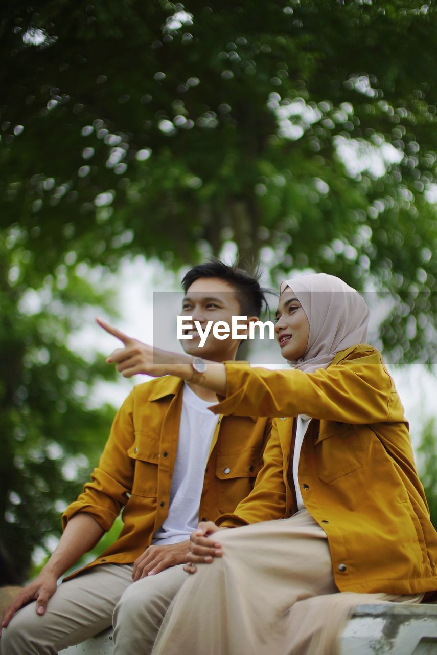 Young couple looking away while sitting against blurred background