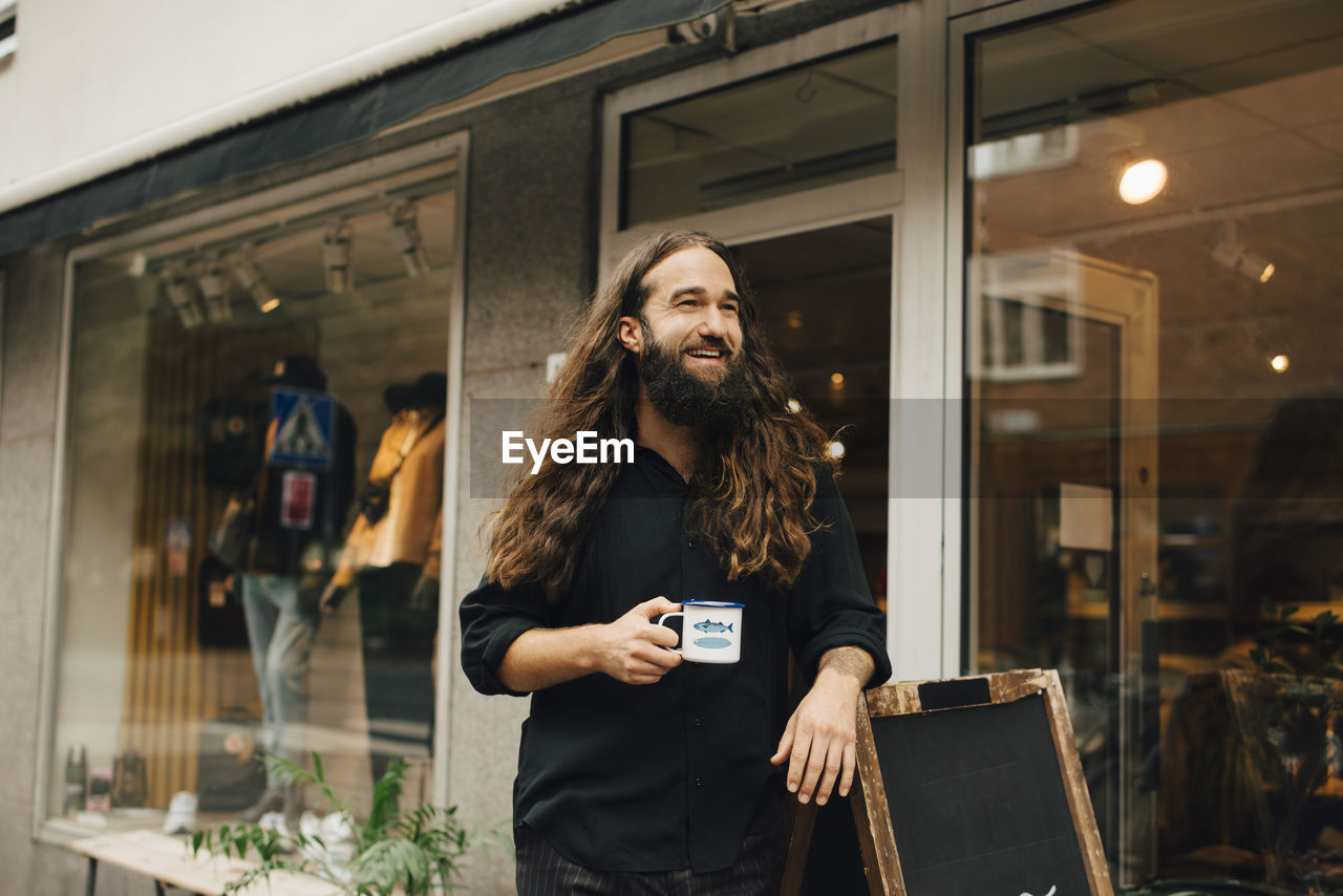 Smiling businessman with coffee cup looking way outside retail store