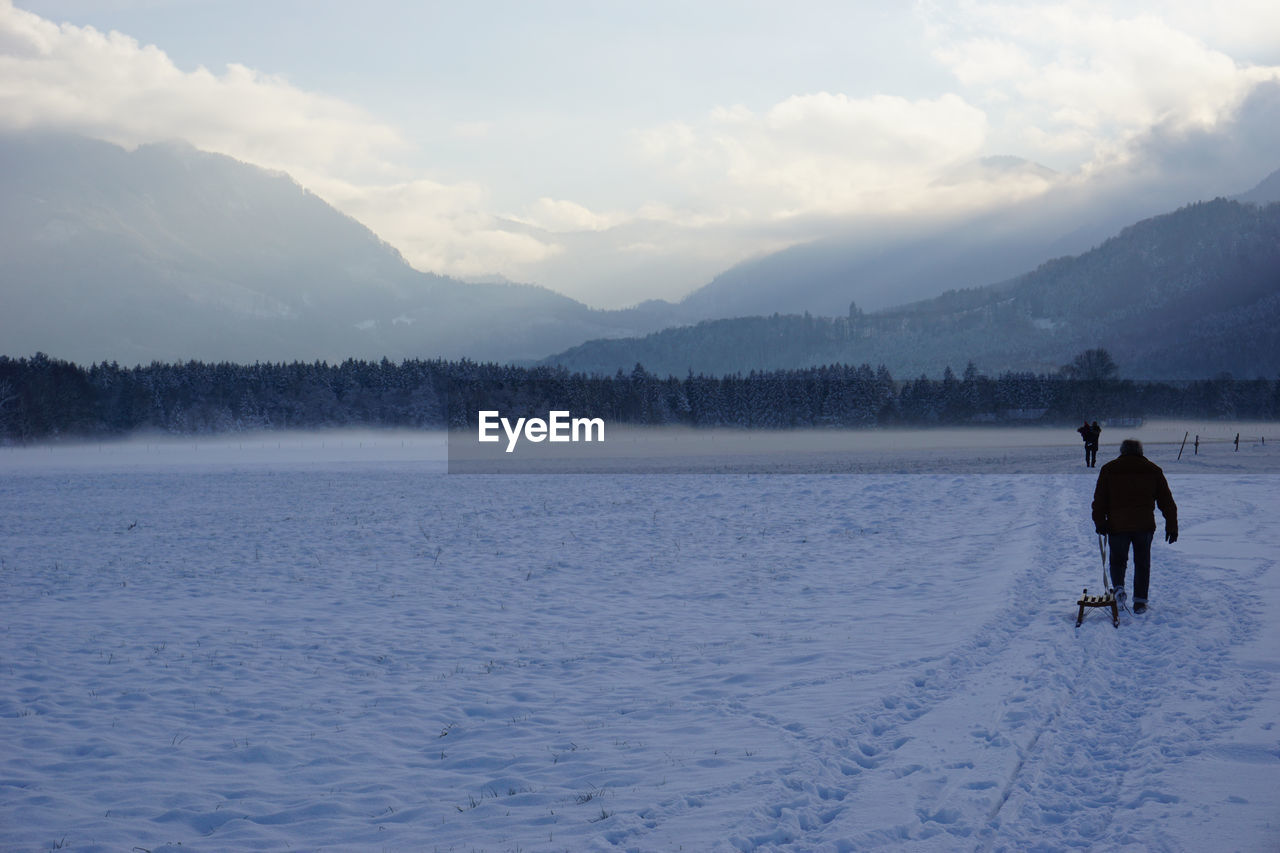 Man carrying sled on snow covered field