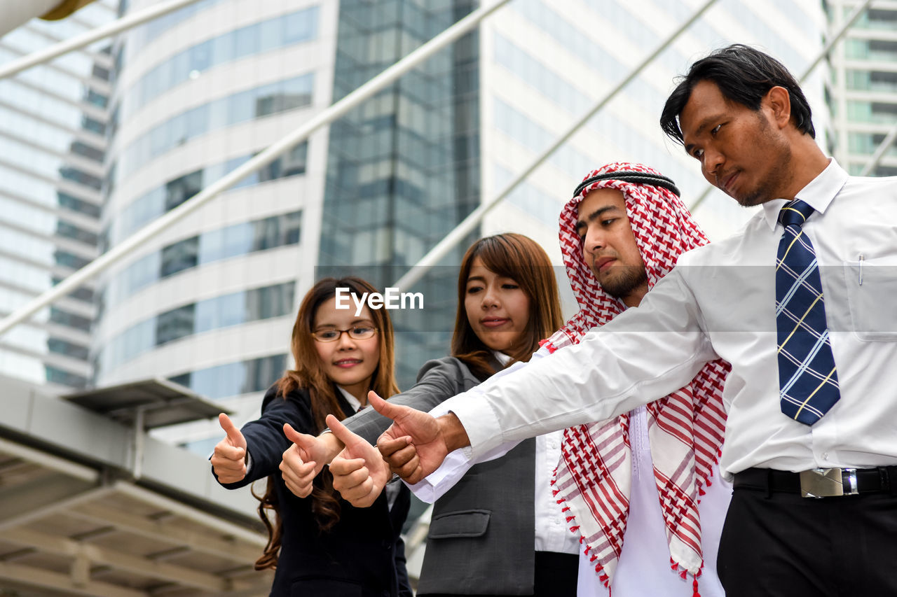 Low angle view of colleagues showing thumbs up against skyscraper in city