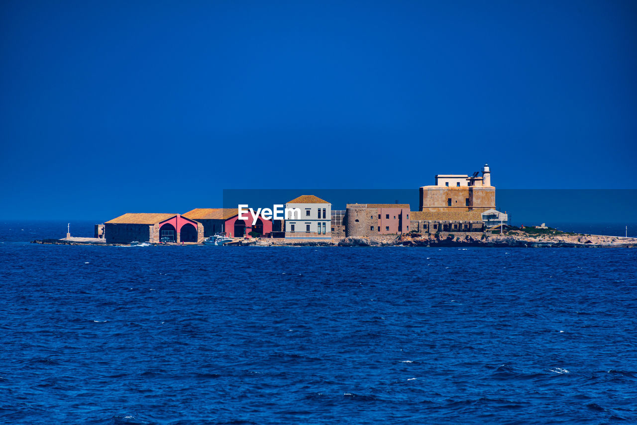 View of buildings by sea against clear blue sky