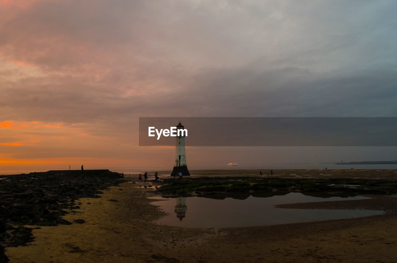 LIGHTHOUSE ON BEACH AGAINST SKY DURING SUNSET