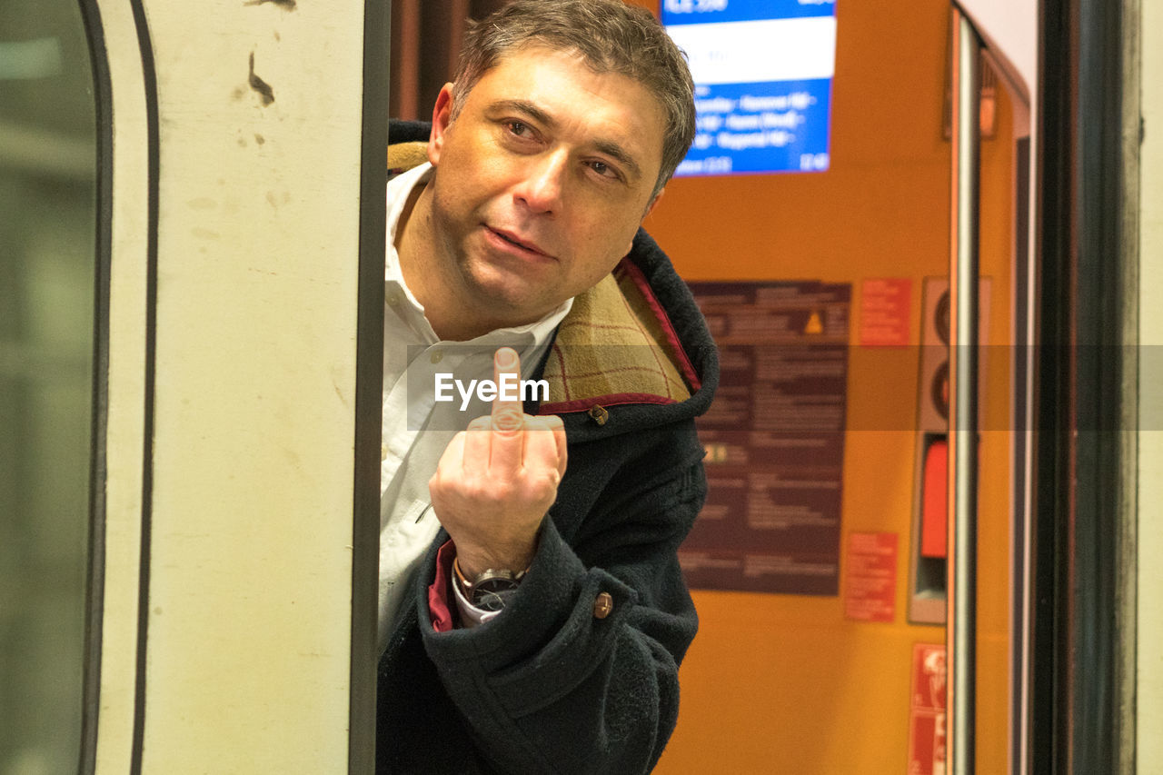 Portrait of man showing obscene gesture while standing in train