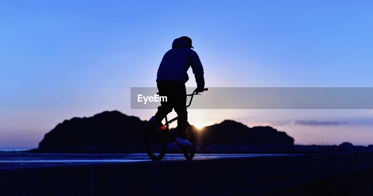 Full length of man cycling at beach against sky during sunset