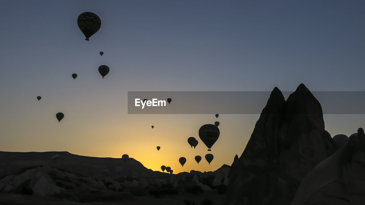 Hot air balloons flying over silhouette landscape against clear sky