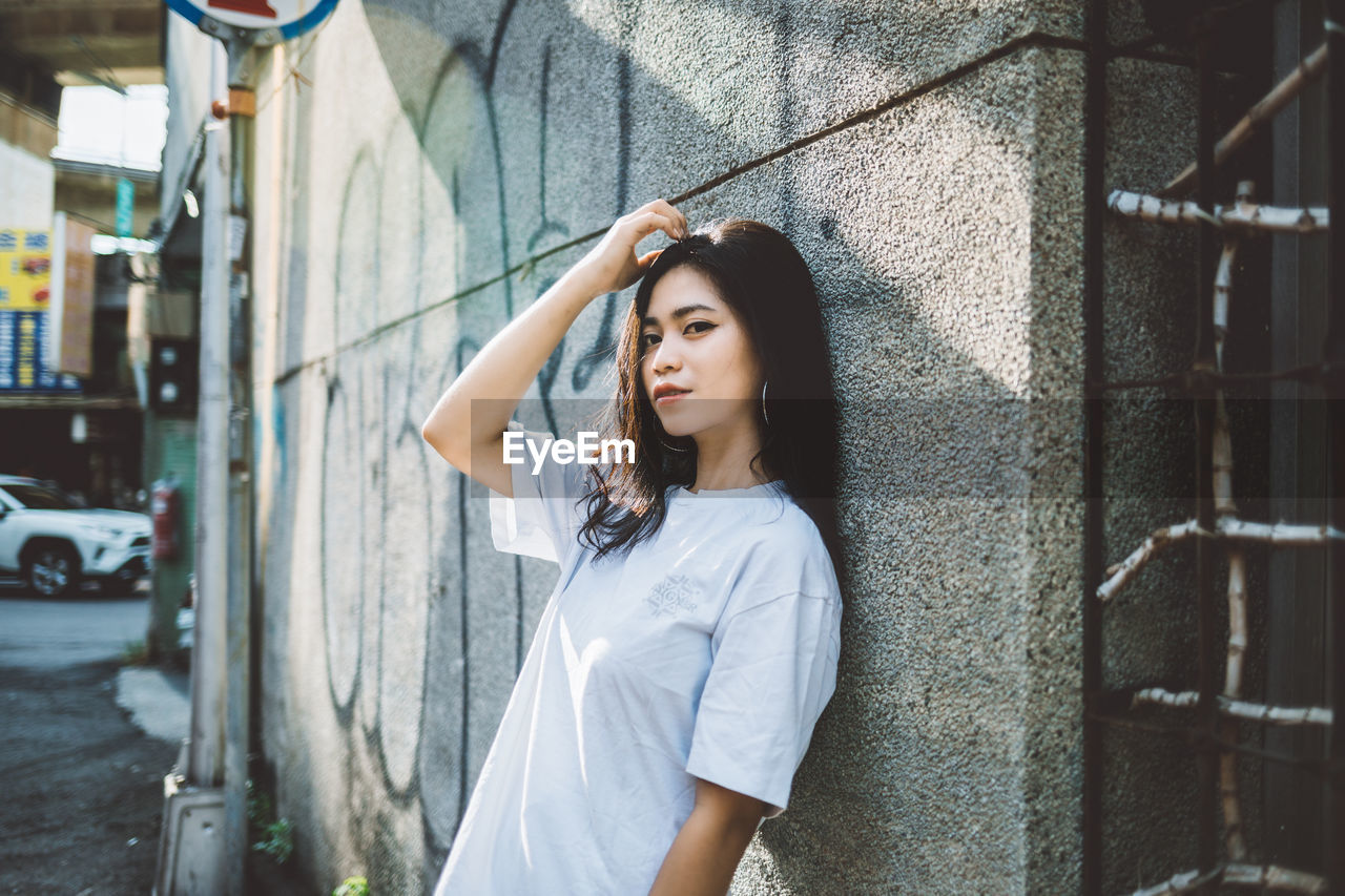 PORTRAIT OF BEAUTIFUL YOUNG WOMAN STANDING AGAINST WALL