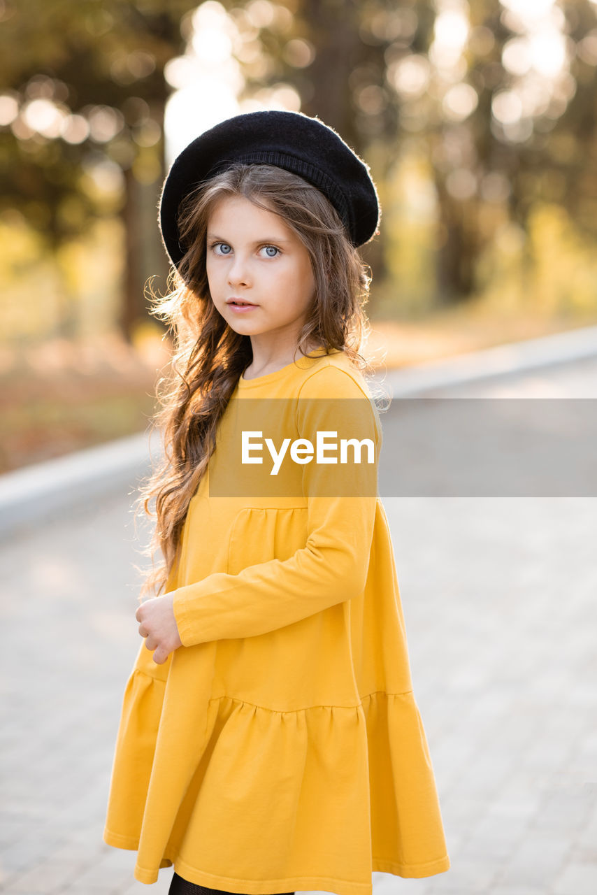 Stylish child girl 5-6 year old wear yellow dress and beret hat in autumn park outdoor.