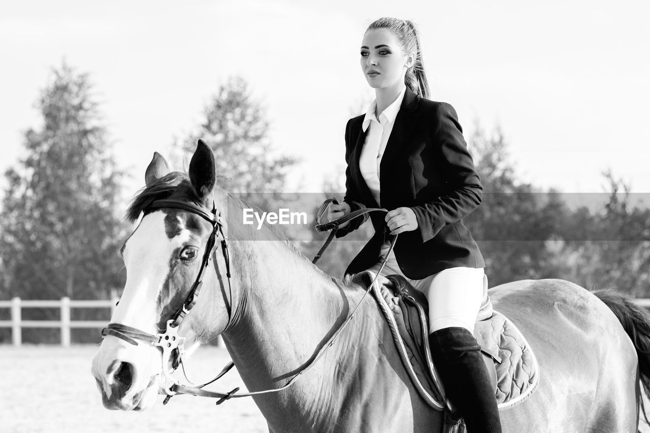 side view of woman riding horse against sky