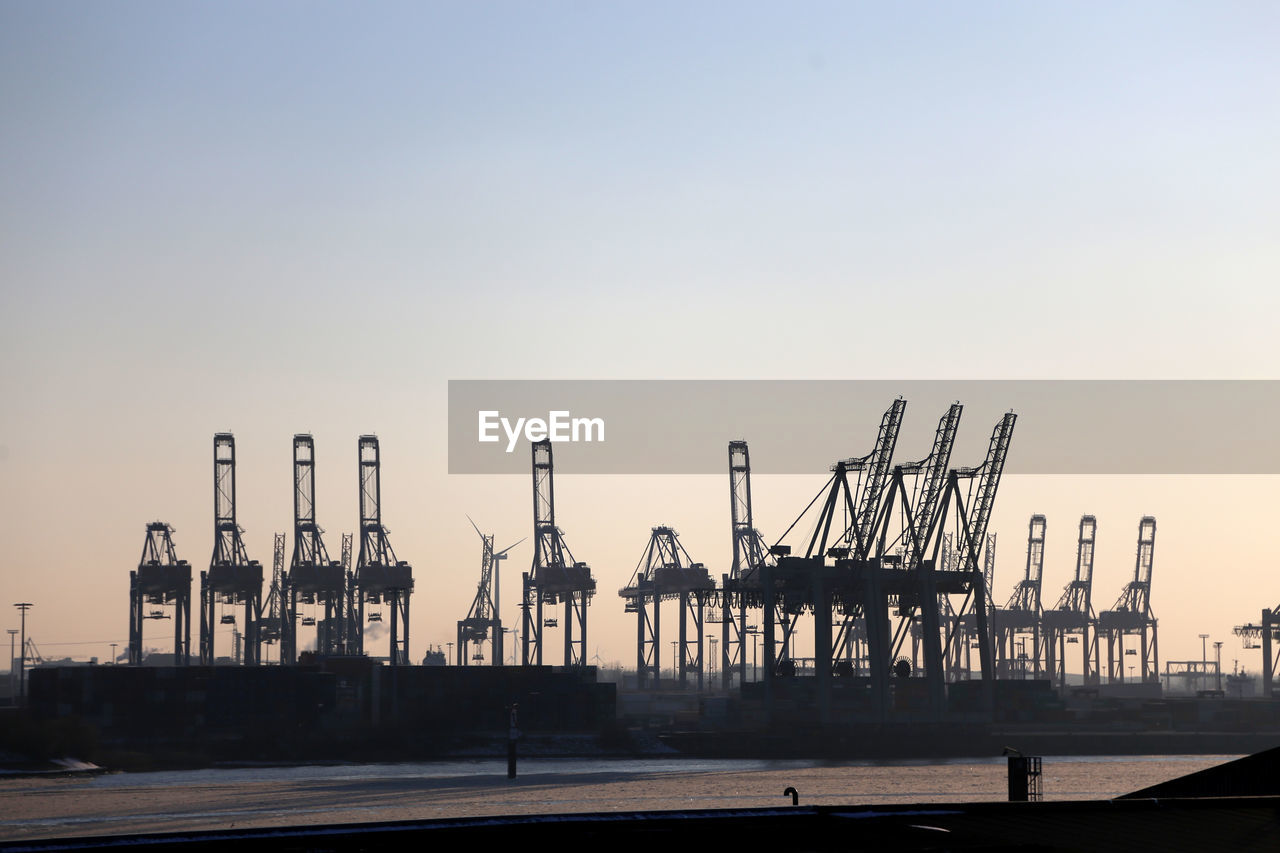 Cranes at harbor against clear sky