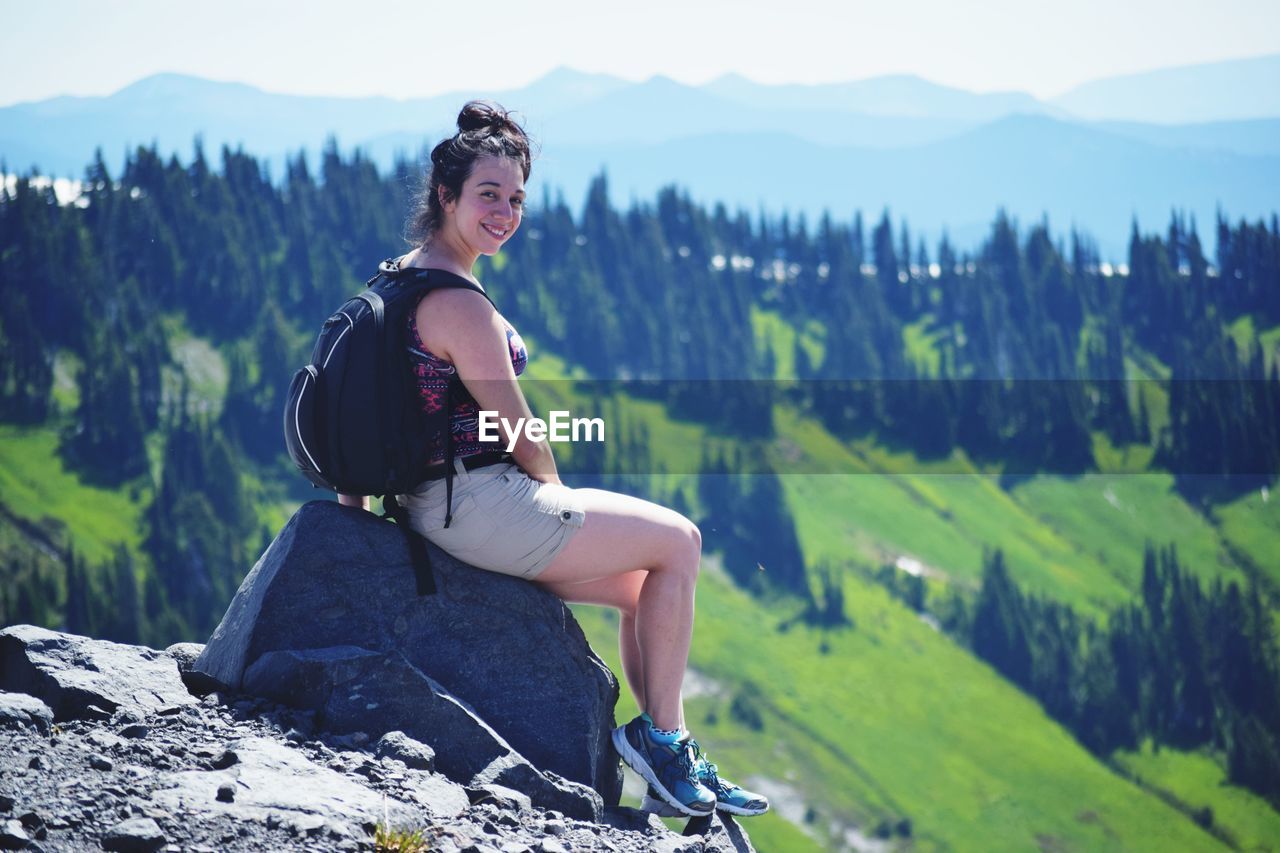 Portrait of young woman sitting on rock against mountains
