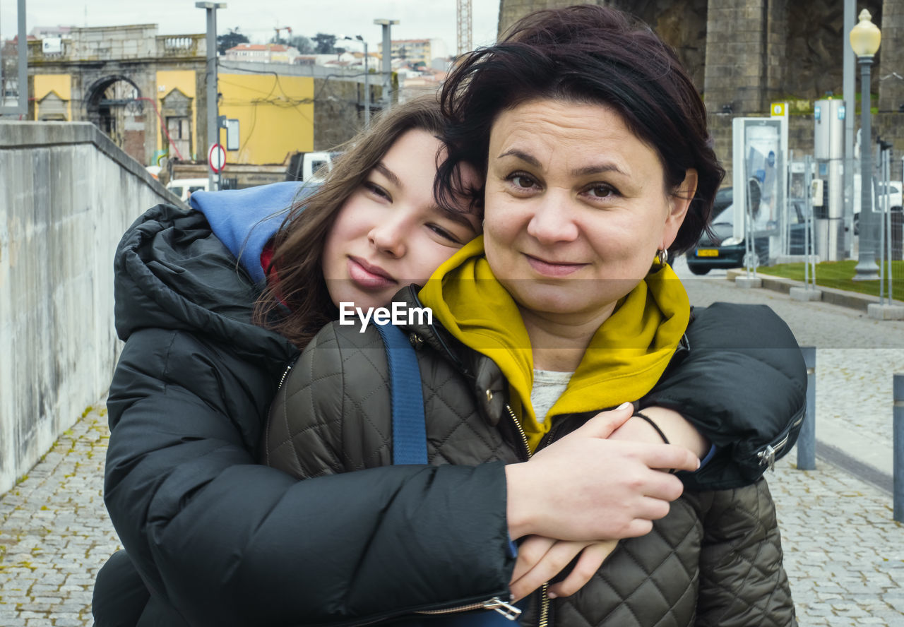 Happy teenage girl hugs her mother while walking on the street