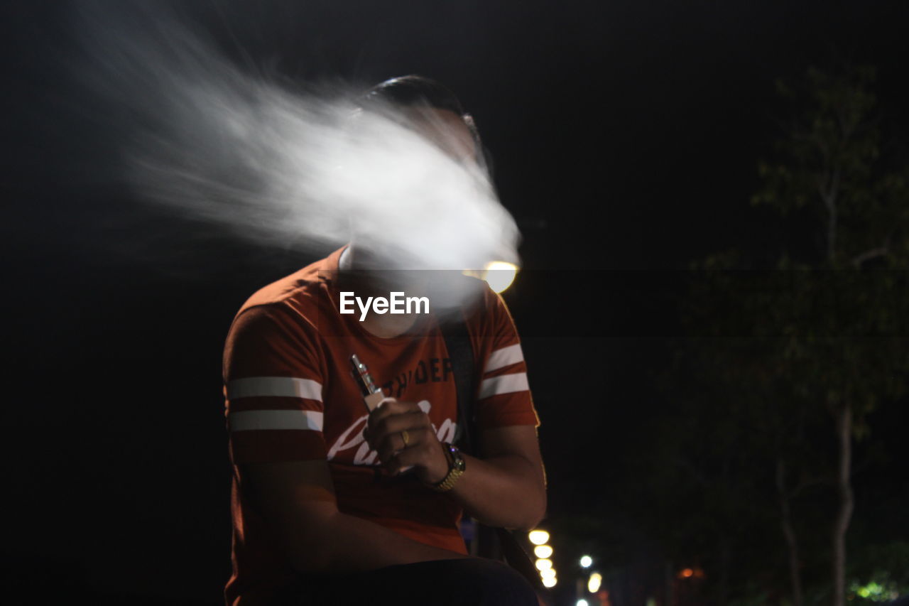 Man emitting smoke while holding cigarette outdoors