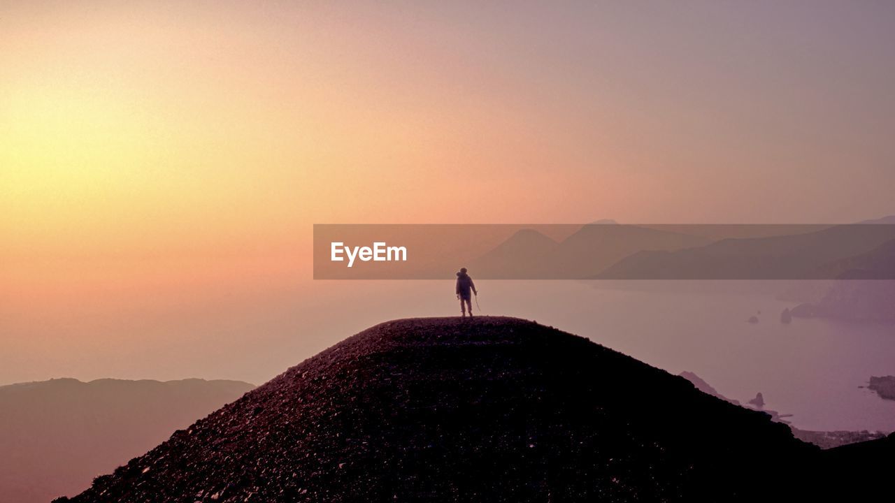 Silhouette man standing on mountain against sky during sunset