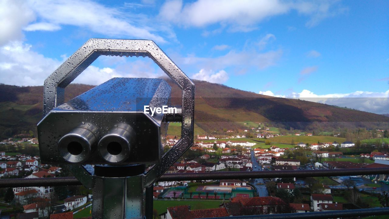 Close-up of wet coin-operated binoculars by residential district against sky during monsoon